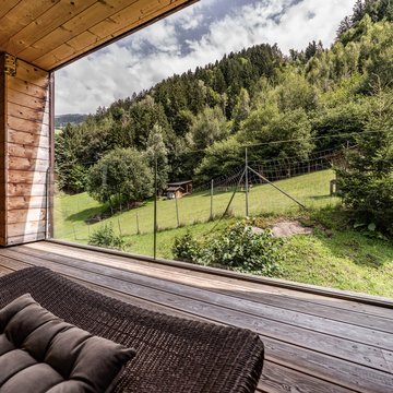 Holiday apartment in Zillertal with panoramic views Wooden terrace with lounge chairs overlooking green hill and forest